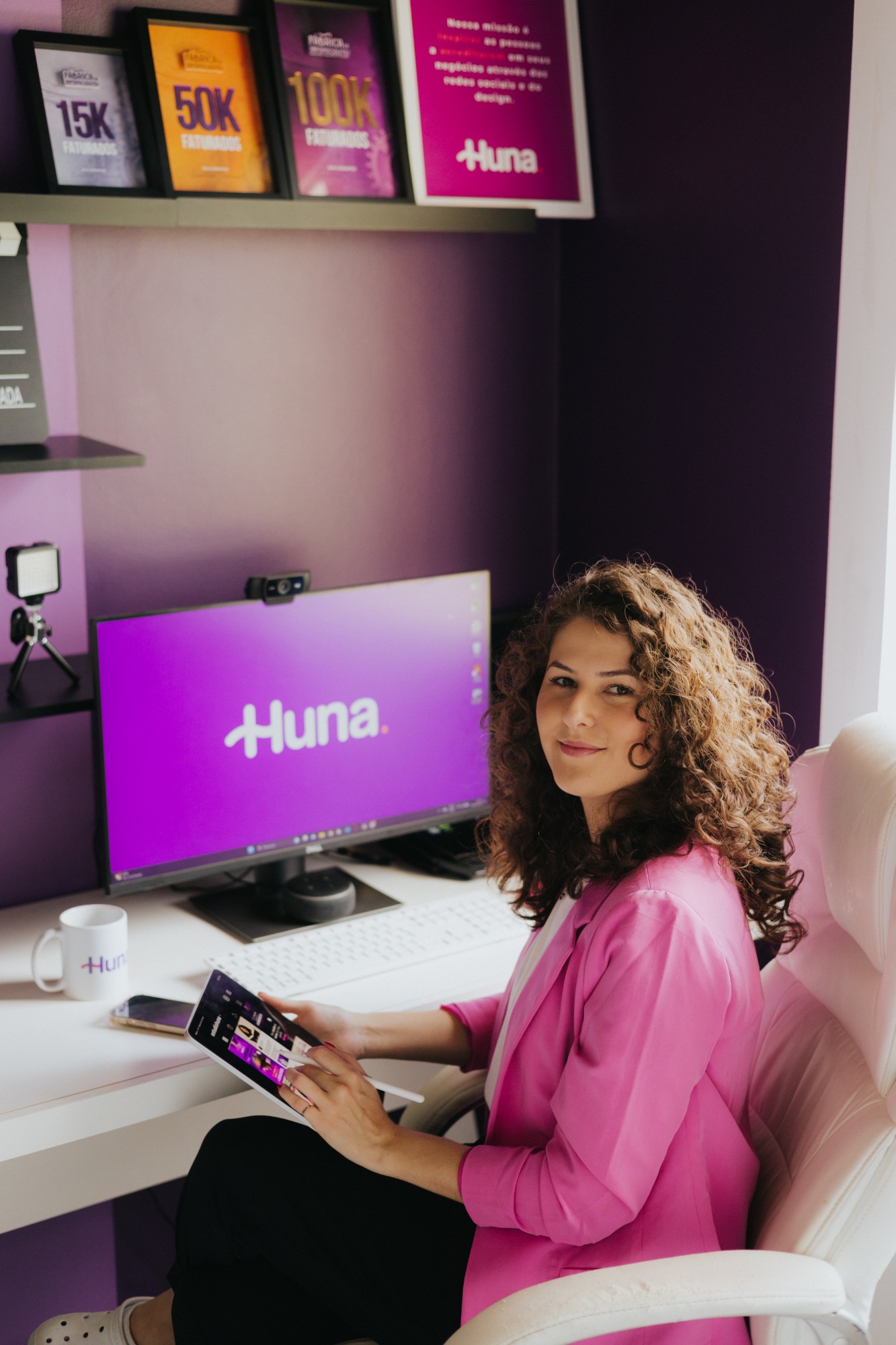 Simara Miguel no escritório do Estúdio Huna, com o logo Huna no monitor